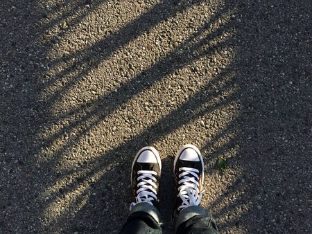 Canvas sneakers shoes on woman's feet on the asphalt with shadow lines. Copy space.