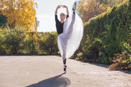 Woman ballerina in a white ballet skirt dancing in pointe shoes in autumn park.の写真素材