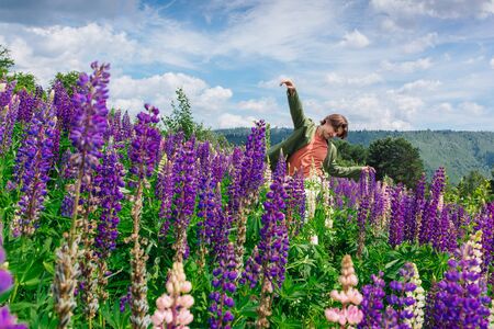 Tall handsome man in a green jacket standing on lupine flowers field, enjoing the beauty of nature. Man surrounded by purple and pink lupines.の写真素材
