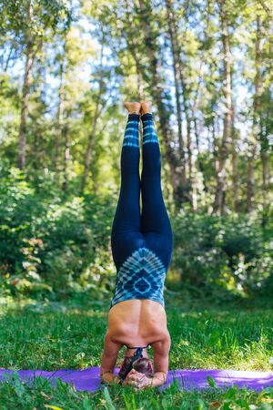 Young caucasian woman doing yoga exercises in summer city park. Woman doing headstand