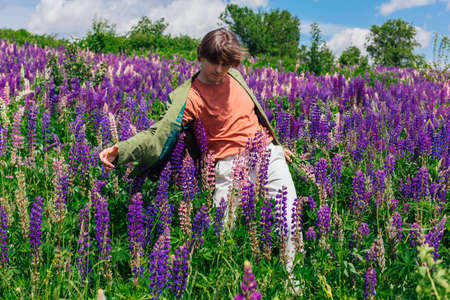 Tall handsome man in a green jacket dancing on lupine flowers field, enjoing the beauty of nature. Man surrounded by purple and pink lupines.の写真素材
