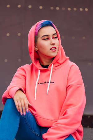 Young girl with short colorful hair and nose piercing dressed in pink hoodie