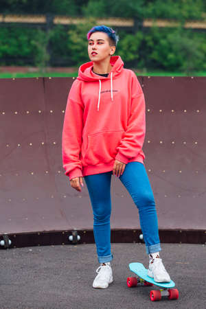 Portrait of a trendy pretty young girl dressed in pink hoodie and jeans standing next to the...