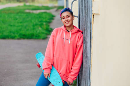 Stylish young woman with short colored hair holding blue plastic skateboard in hand. Youth concept.の写真素材