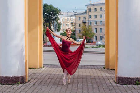 Woman ballerina in red ballet dress dancing in pointe shoes next to the old columns. Ballerina standing in beautiful ballet poseの写真素材