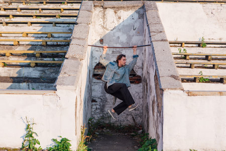 Fashion portrait of a tall handsome man dressed in jeans jacket on the crushed tribune of the old stadium during sunsetの写真素材