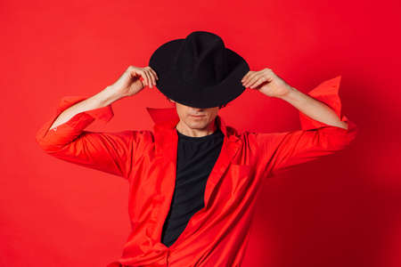 Portrait of a tall handsome man dressed in red shirt and black hat posing on the red background.の写真素材