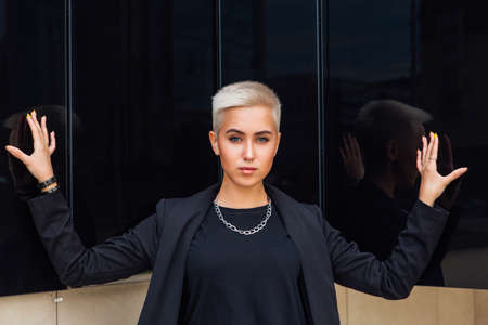 Young stylish business woman with short hair and nose piercing. Confident girl look like lesbian standing near business center with mirror wallsの写真素材