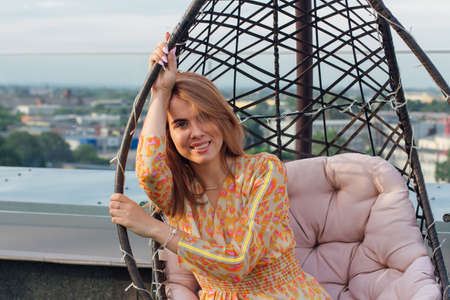 Beautiful young woman in long leopard dress sitting on a swing on the top of the roof of a building.