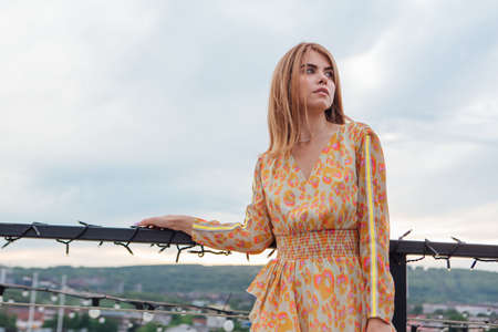 Beautiful young woman in long leopard dress standing on the stairs on the top of the roof of a...