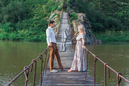 Beautiful young romantic couple standing on the suspension bridge above the riverの写真素材