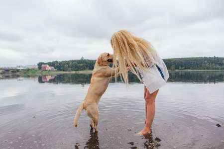 Young beautiful woman with blond curly hair playing with her labrador retriever dog in river.の写真素材