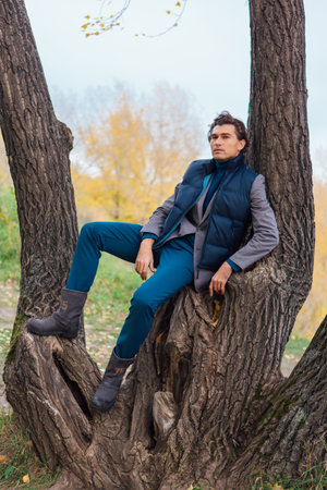 Tall handsome man climbing on the tree in autumn forestの写真素材