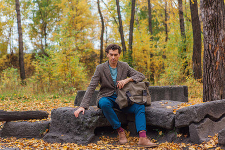Tall handsome man with a bag sitting on the rocks in the autumn forestの写真素材