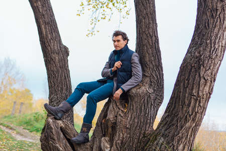 Tall handsome man climbing on the tree in autumn forestの写真素材