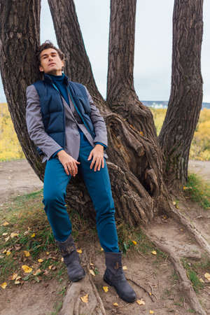 Tall handsome man standing near the tree in autumn forestの写真素材