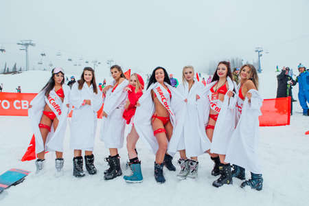 Young happy pretty women in red bikinis and white bathrobes on the snow slope.のeditorial素材