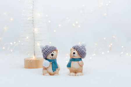 Decorative Christmas-themed figurines. The statuette of a cat and a bear in a knitted hat on the white background. Festive decor, warm bokeh lightsの写真素材