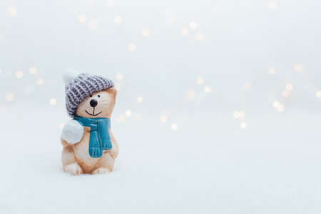 Decorative Christmas-themed figurines. The statuette of a cat with a snowball in a knitted hat on the white background. Festive decor, warm bokeh lightsの写真素材