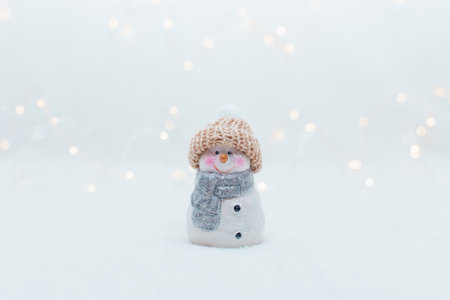 Decorative Christmas-themed figurines. The statuette of a snowman in a knitted hat on the white background. Festive decor, warm bokeh lightsの写真素材