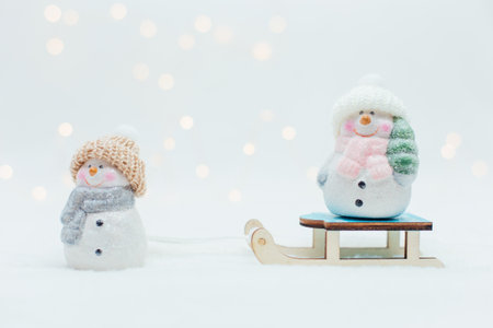 Decorative Christmas-themed figurines. Two statuette of a snowmen in a knitted hat on the sledge. Festive decor, warm bokeh lightsの写真素材