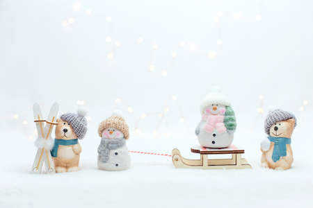 Decorative Christmas-themed figurines. The statuette of a cat, penguin and a bear with ski and a snoman on the sledge. Cute animals in a knitted hat on the white background. Warm bokeh lightsの写真素材