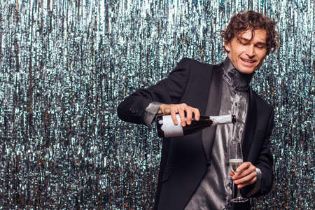 Happy tipsy man with bottle of champagne and wine glass at christmas or new year party on a sparkle background.の写真素材