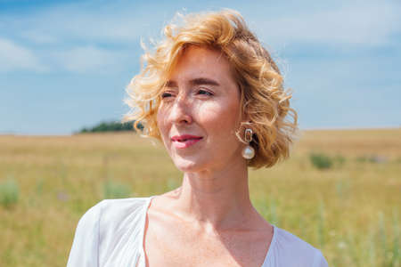 Beautiful blonde woman with short curly hair outdoors. Romantic model in summer white dress.の写真素材