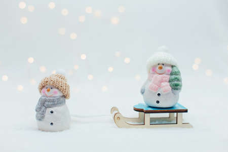 Decorative Christmas-themed figurines. Two statuette of a snowmen in a knitted hat on the sledge. Festive decor, warm bokeh lightsの写真素材
