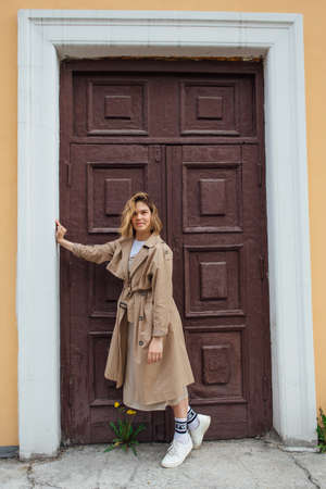 Young smiling millennial woman with wild hair dressed in an autumn coat posing near the door of an old building.の写真素材