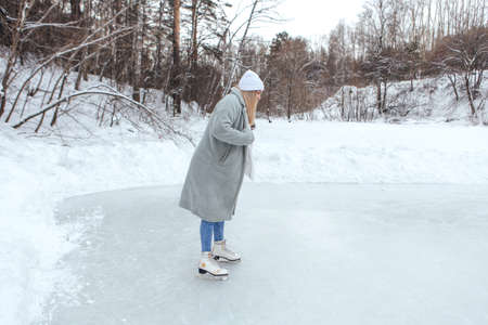 Lovely young woman riding ice skates on the ice rink. Girl skating on ice in a winter frosty day