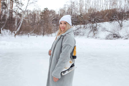 Lovely young woman with ice skates on the ice rink. Girl is going to skating on ice in a winter frosty dayの写真素材
