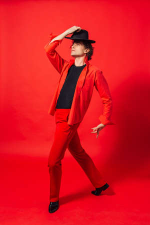 Portrait of a tall handsome man dressed in red shirt and black hat posing on the red background.の写真素材