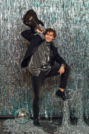Tall attractive man holding electro guitar standing over the sparkle background with a mirror disco ball on the floor. party concept.の写真素材