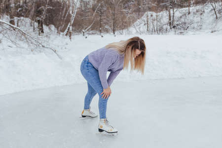 Lovely young woman riding ice skates on the ice rink. Girl skating on ice in a winter frosty day