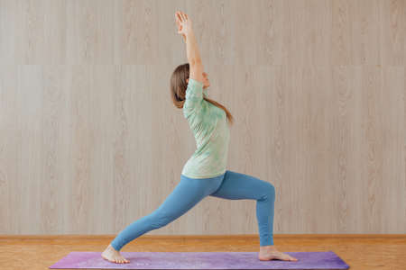 Young caucasian woman dressed in a blue leggins and t-shirt doing yoga asanas at home. Fitness and healthy lifestyle concept.の写真素材