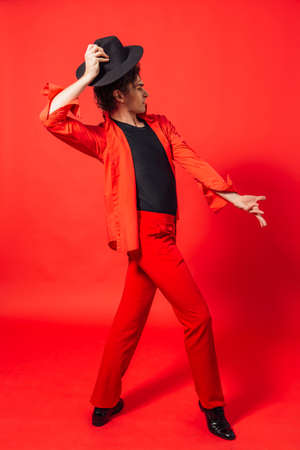 Portrait of a tall handsome man dressed in red shirt and black hat posing on the red background.の写真素材