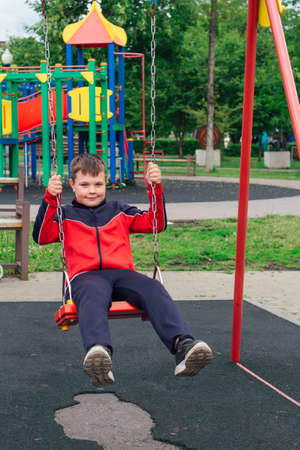 Outdoors portrait of a cute boy swinging on a swing at the playground in a park.の写真素材