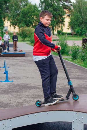 Cute boy riding scooter in a summer park. Happy teenager riding a modern scooter.の写真素材