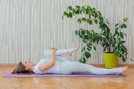 Young caucasian woman dressed in a blue leggins and t-shirt doing yoga asanas at home. Fitness and healthy lifestyle concept.の写真素材
