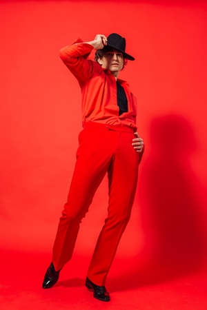 Tall handsome man dressed in red shirt and black hat posing on the red backgroundの写真素材