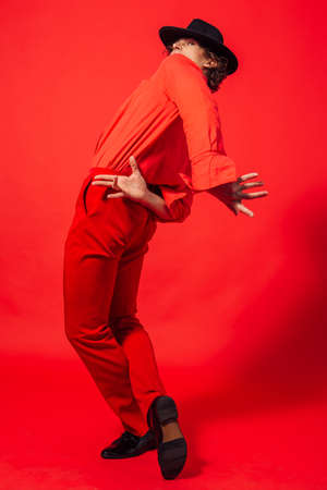 Tall handsome man dressed in red shirt and black hat posing on the red backgroundの写真素材