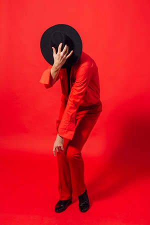 Tall handsome man dressed in red shirt and black hat posing on the red backgroundの写真素材