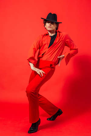Portrait of a tall handsome man dressed in red shirt and black hat posing on the red background.の写真素材