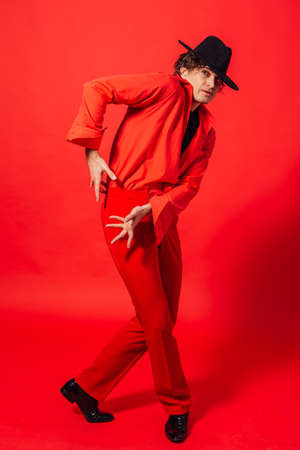 Portrait of a tall handsome man dressed in red shirt and black hat posing on the red background.の写真素材