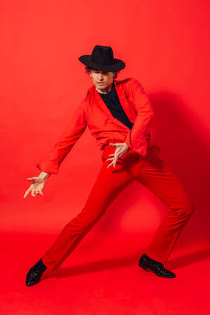 Portrait of a tall handsome man dressed in red shirt and black hat posing on the red background.の写真素材