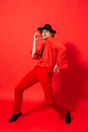 Portrait of a tall handsome man dressed in red shirt and black hat posing on the red background.の写真素材