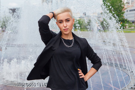 Young stylish business woman with short hair and nose piercing. Confident girl look like lesbian standing near fountainの写真素材