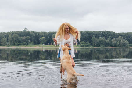 Young beautiful woman with blond curly hair playing with her labrador retriever dog in river.の写真素材