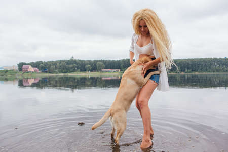 Young beautiful woman with blond curly hair playing with her labrador retriever dog in river.の写真素材